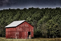 An old red barn at the edge of a forest