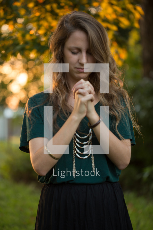 a woman with praying hands outdoors 