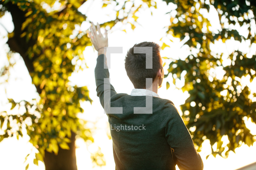 Back of a man standing outside with his arm raised in praise.