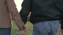 Adult middle aged couple holding hands, walking together outside at sunset.
