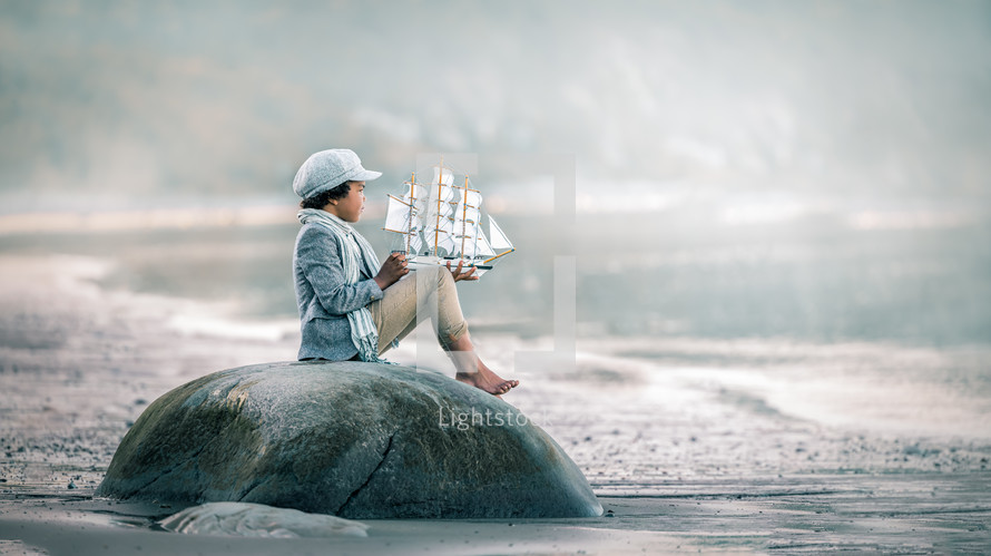 a boy sitting on a rock playing with a toy boy 