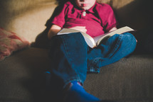 a kid reading a Bible on a couch 