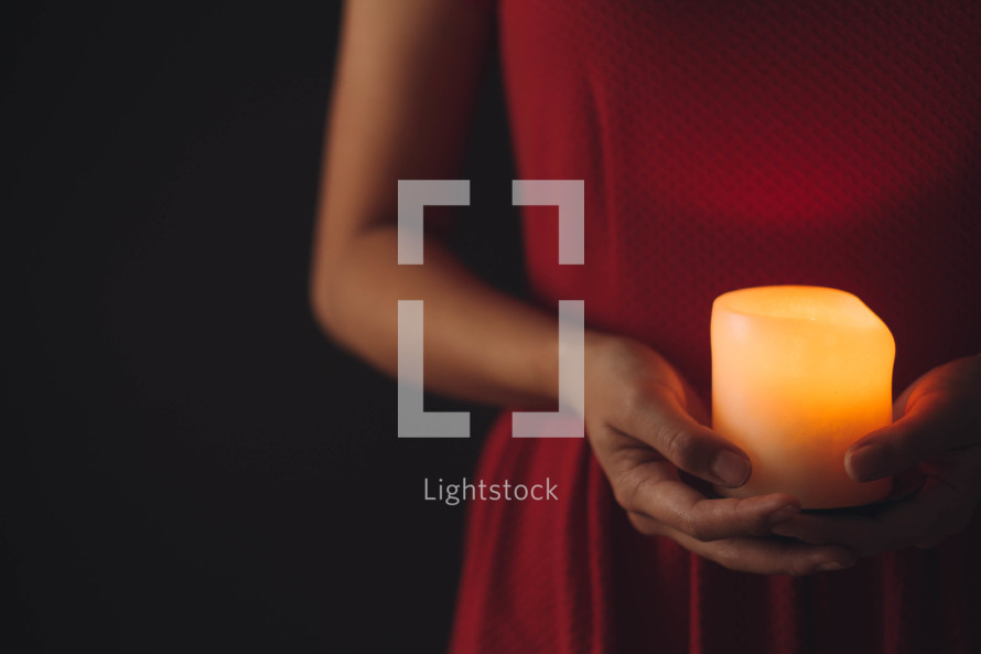 A woman in a red dress holds a lit candle.