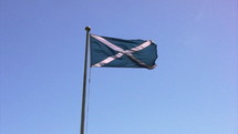Blue flag with a white X on it, blowing in the wind from a flag pole