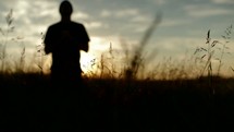 A man praying and worshiping in a field at sunrise