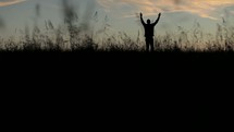 Silhouette of a man praising His name in a field at daybreak.