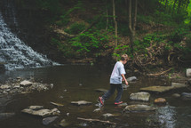 a boy walking over rocks in a creek 