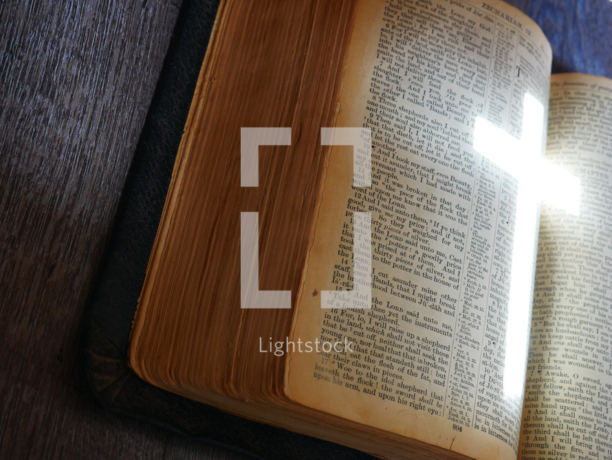 light in the shape of a cross on the pages of a Bible 