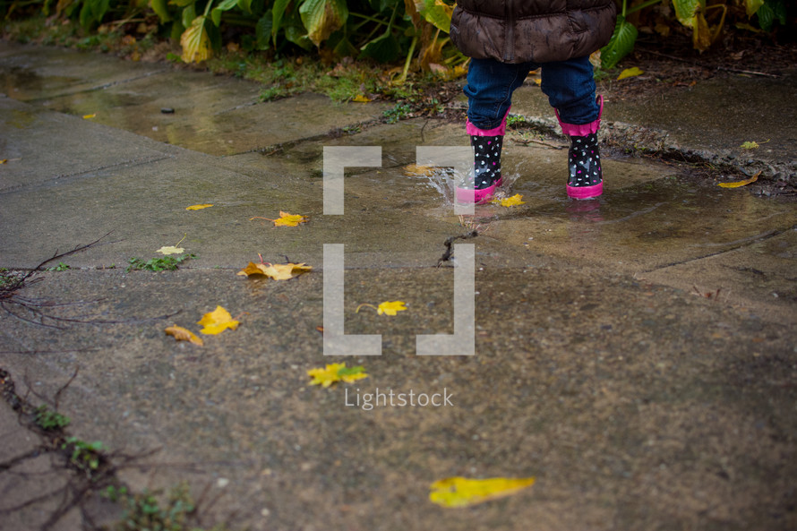 a toddler in rain boots splashing in a puddle 