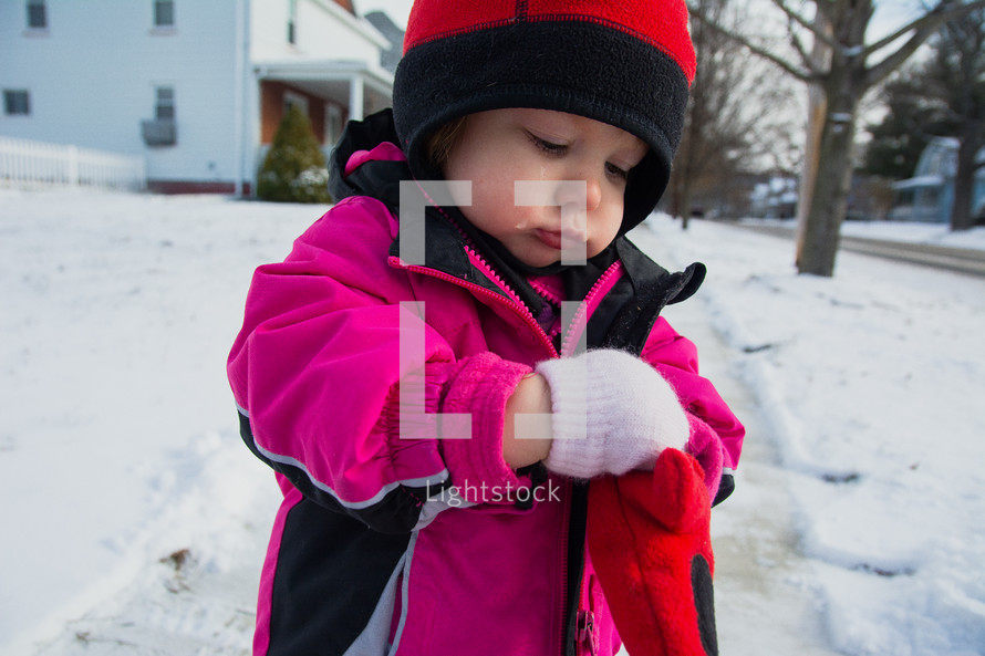a toddler girl in a winter coat and mittens standing in the snow 