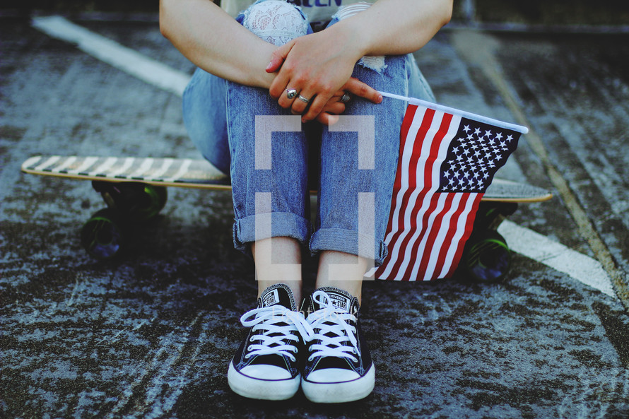 teen sitting on a skateboard holding an American flag 
