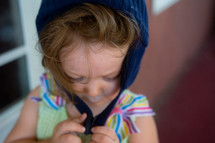 a toddler girl fastening a winter hat in summer 