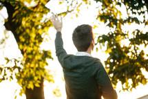 Back of a man standing outside with his arm raised in praise.
