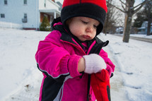 a toddler girl in a winter coat and mittens standing in the snow 