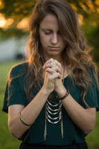 a woman with head bowed and praying hands outdoors 