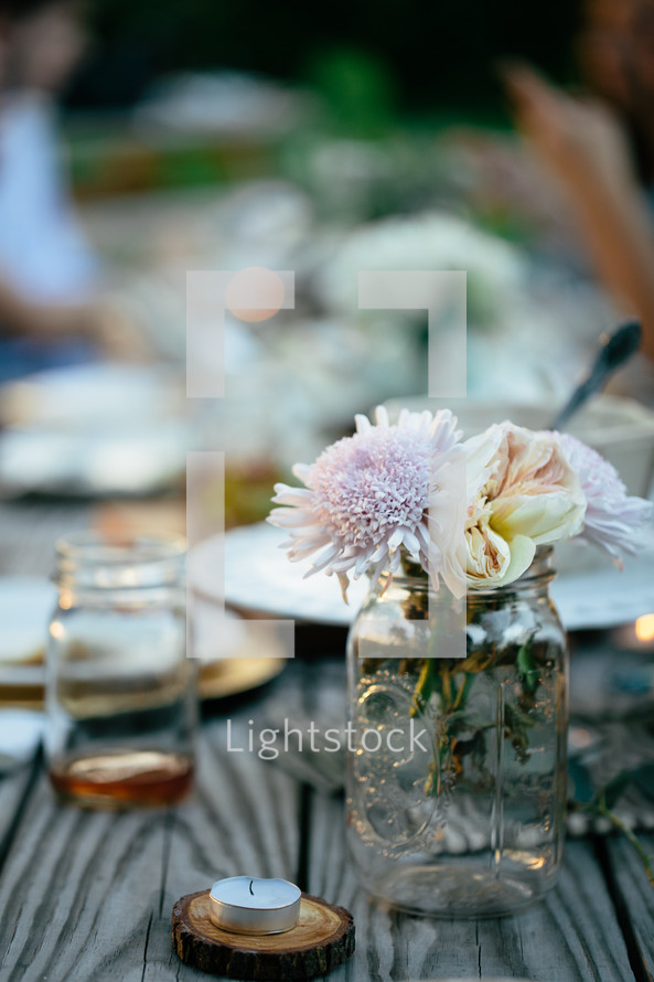 flowers in a mason jar vase at a table and a tea candle 