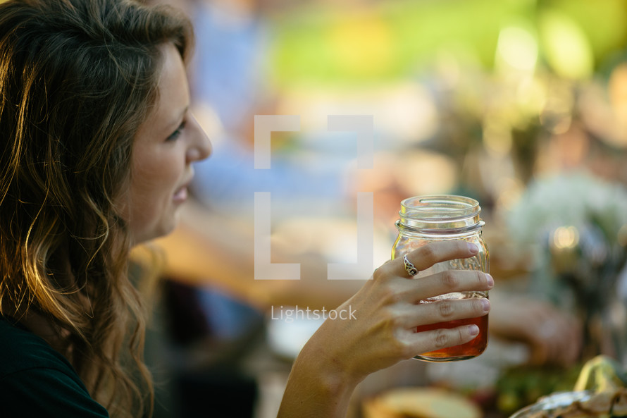 a woman drinking out of a mason jar glass 