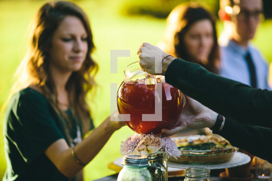 pouring tea from a pitcher and a family at a dinner table outdoors 