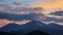 Timelapse of clouds moving near a mountain peak at sunset. 