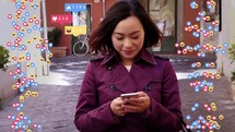 Woman walking looking down at her phone with animated social media emojis,