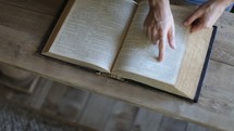 Aerial view of hands flipping the pages of a Bible.