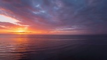 Timelapse of the sun setting over the ocean on a cloudy day as night falls.