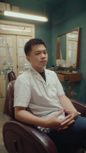 Young Asian Man Sitting in Barbershop Posing for Camera