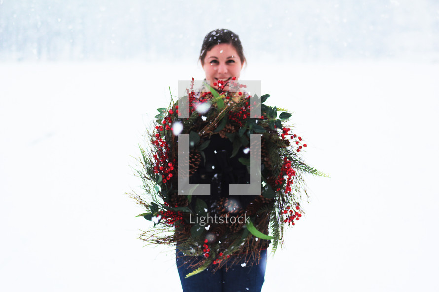 a woman standing in the snow holding a Christmas wreath 