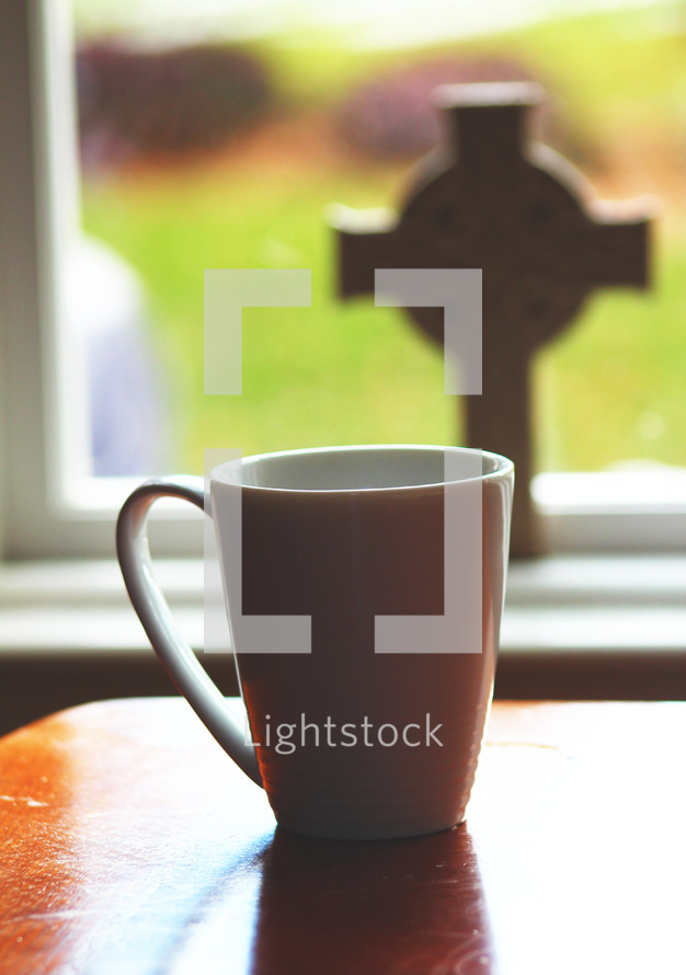 coffee mug on a table and cross in a window 
