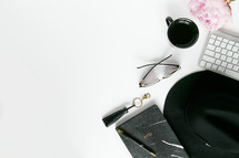 a border of a hat, pen, keychain, sunglasses, mug, and computer keyboard on a woman's desk 