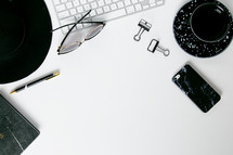 border of a hat, sunglasses, pen, clips, computer keyboard, and cellphone on a white background 