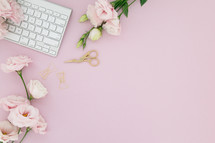 A white computer keyboard on a pink background with pink flowers.