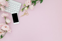 A computer keyboard, cell phone and flowers on a pink background.