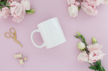 A white coffee cup on a pink background surrounded by pink flowers.