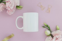 A white coffee cup on a pink background surrounded by pink flowers.
