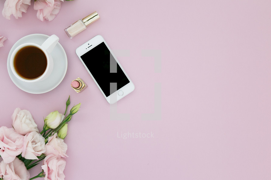 Cup of coffee, lipstick, cellphone and pink flowers on a pink background.