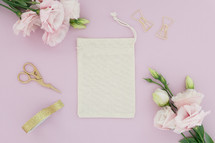 A linen pouch on a pink background surrounded by pink flowers.