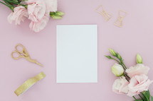A blank white note card on a pink background surrounded by pink flowers.