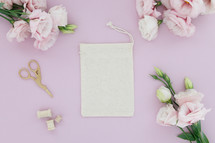 A linen pouch on a pink background surrounded by pink flowers.