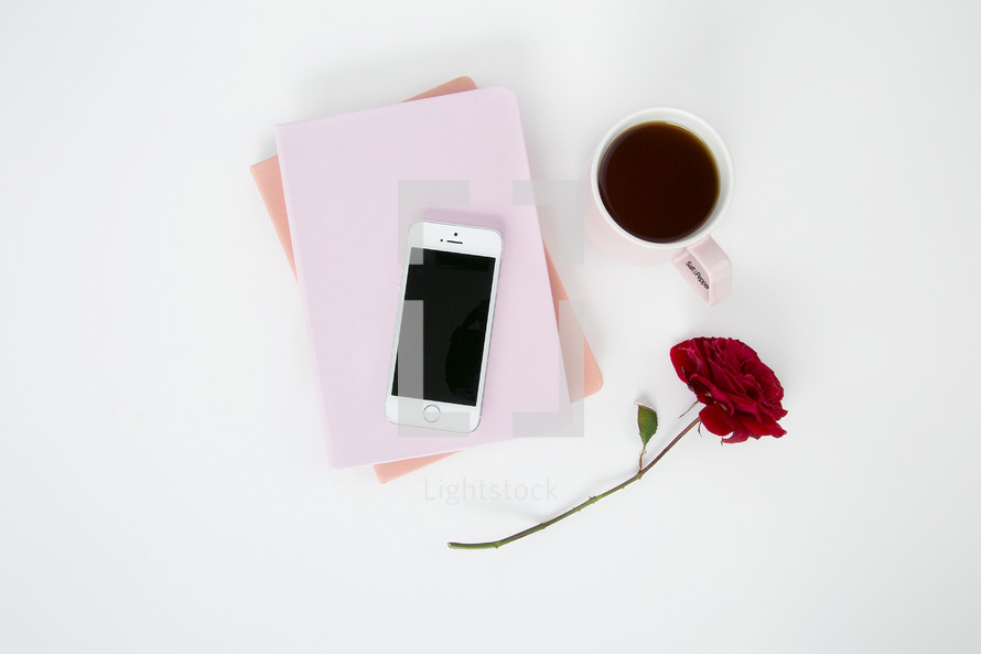 an iPhone on pink journals, red rose, and mug 