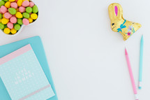 egg shaped candy in a heart shaped bowl, pencils, and journal chocolate bunny, and sunglasses on desk 