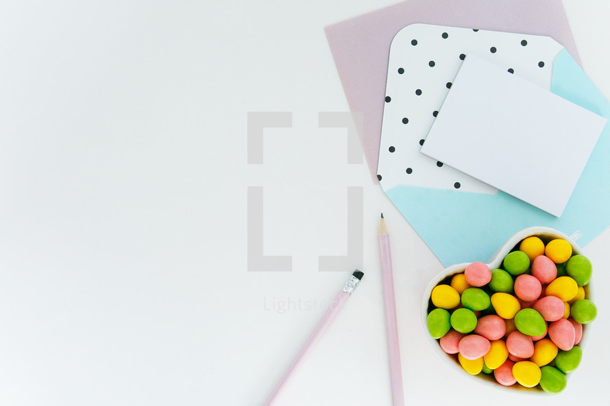 egg shaped candy in a heart shaped bowl, pencils, and stationary on desk 