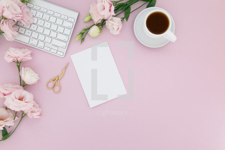 paper, computer keyboard, coffee cups, pink roses and gold scissors on a pink background 