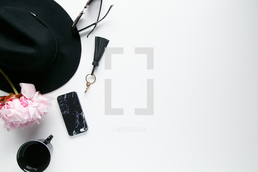 border of a hat, sunglasses, mug, flowers, and cellphone on a white background 