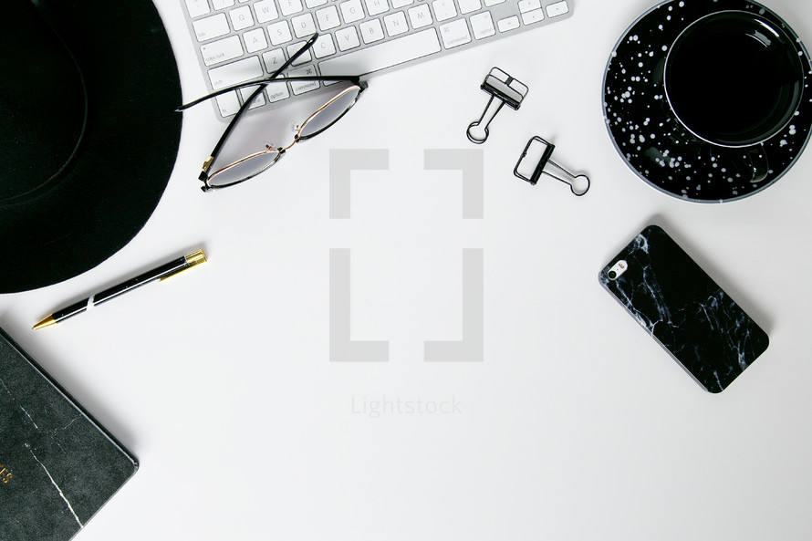 border of a hat, sunglasses, pen, clips, computer keyboard, and cellphone on a white background 