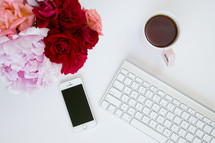 iPhone, computer keyboard, mug, and flowers on a white background 