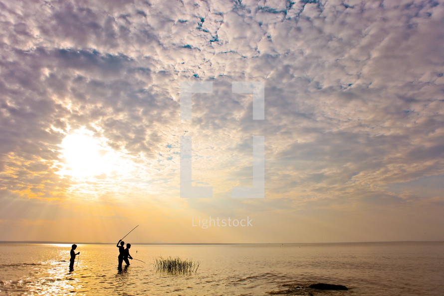 Children wading and fishing during a sunrise