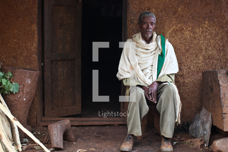 Elderly African man sitting outside of hut