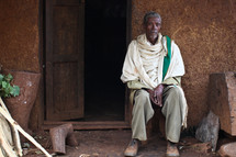 Elderly African man sitting outside of hut