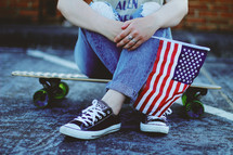 a teen sitting on a skateboard holding an American flag 